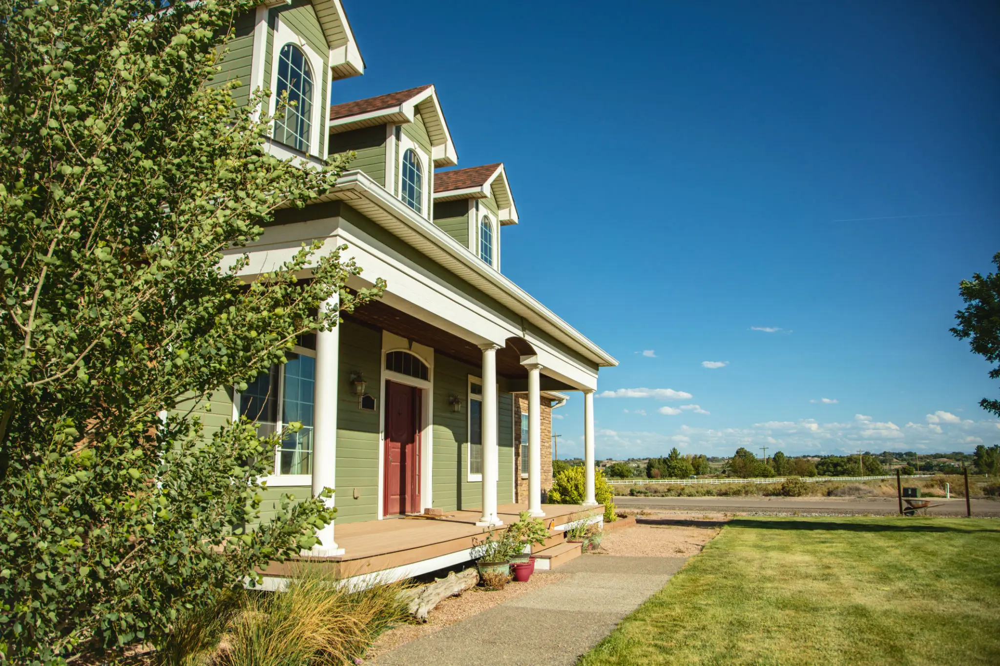 Green house with porch under clear sky.
